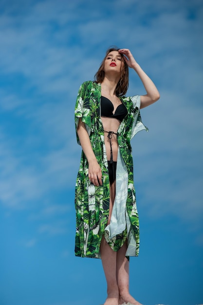 Une femme en kimono vert se tient devant un ciel bleu.