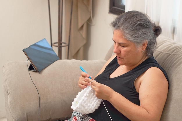 Femme latina mature tricote à la maison en apprenant l'artisanat en ligne