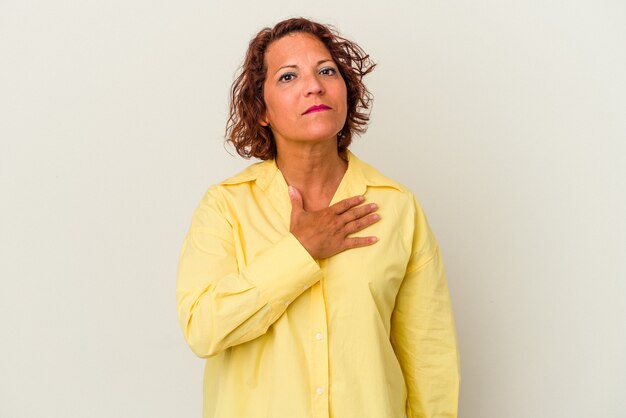 Femme latine d'âge moyen isolée sur fond blanc prêtant serment, mettant la main sur la poitrine.