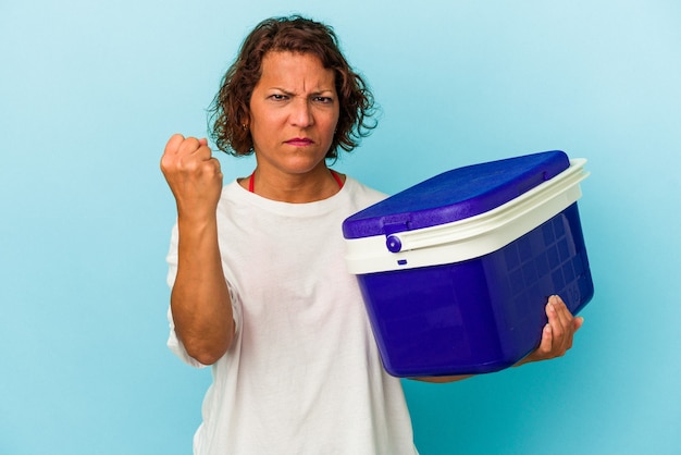 Femme latine d'âge moyen isolée sur fond bleu montrant le poing à la caméra, expression faciale agressive.