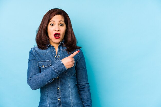 Femme latine d'âge moyen isolée sur fond bleu pointant vers le côté