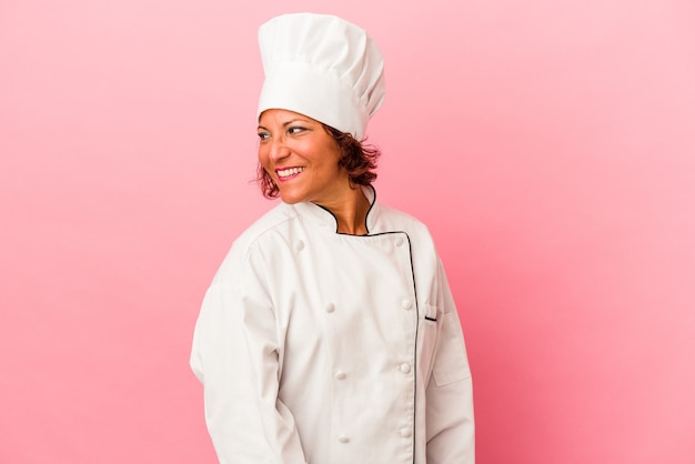 Une femme latine d'âge moyen isolée sur fond rose regarde de côté souriante, gaie et agréable.