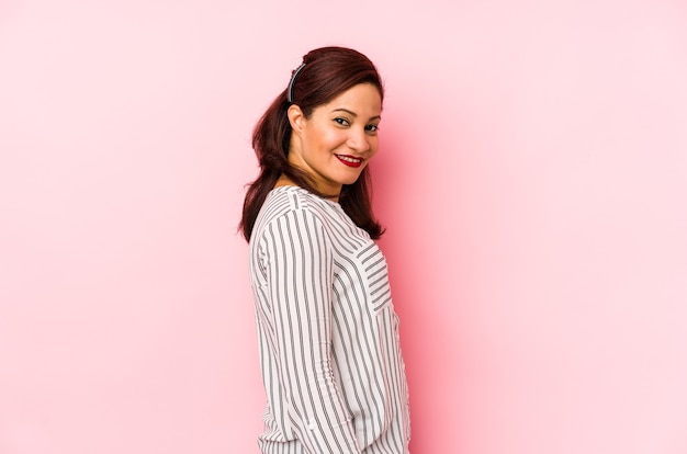 Femme latine d'âge moyen isolée sur un mur rose regarde de côté souriant, joyeux et agréable