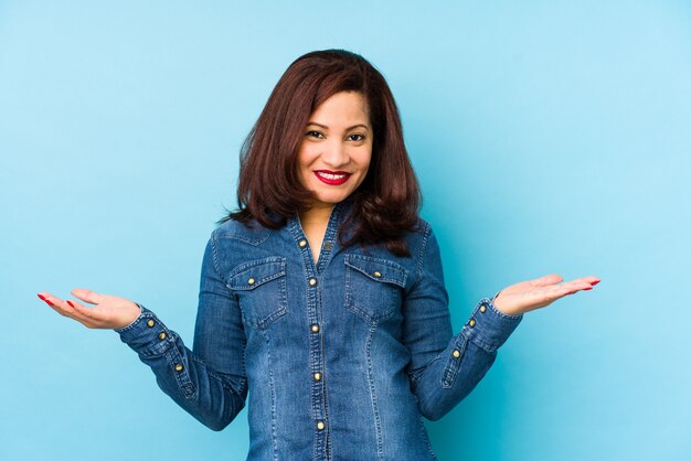 Femme latine d'âge moyen sur un mur bleu montrant une expression bienvenue.