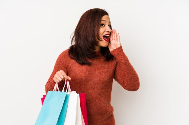 Femme latine d'âge moyen tenant un sacs à provisions isolé criant et tenant la paume près de la bouche ouverte.