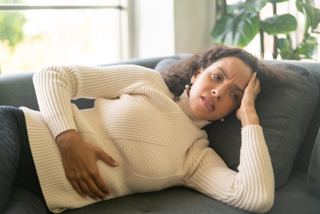 Femme latine allongée sur un canapé à la maison avec un sentiment de mal de tête