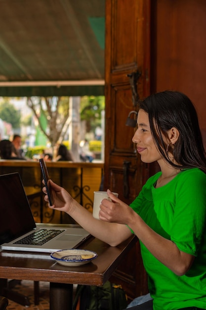 Femme latine assise dans un vieux café vérifiant son téléphone portable tout en buvant une tasse de café