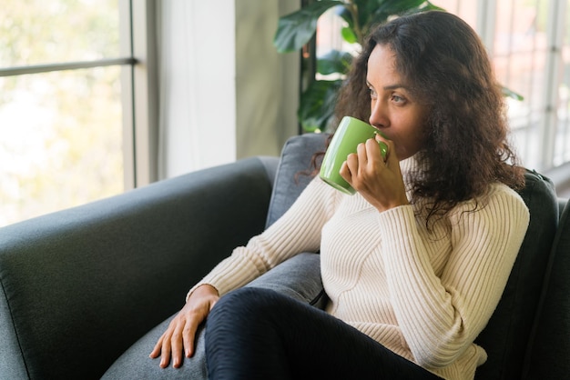 Femme latine buvant du café sur un canapé à la maison