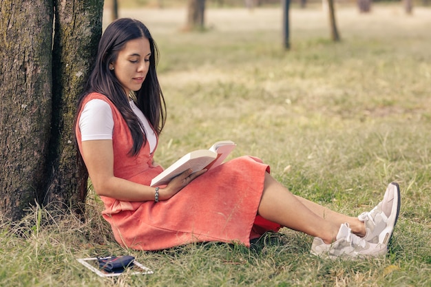 Femme latine lisant un livre orné d'un arbre dans le parc