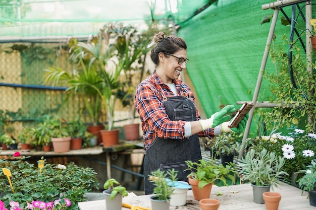 Femme latine mûre travaillant à l'intérieur du jardin à effet de serre à l'aide d'une tablette numérique