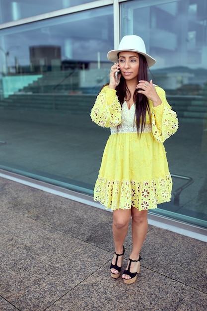 Femme latine en robe jaune parlant au téléphone dans la rue.