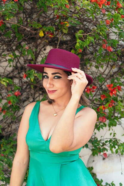 Femme latine en robe verte et chapeau rouge, debout dans le parc.