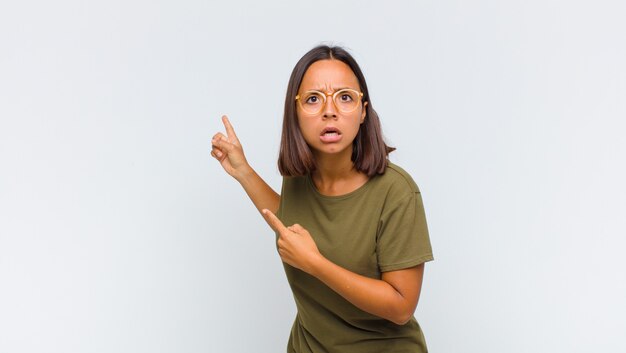 Femme latine se sentant choquée et surprise, pointant vers l'espace de copie sur le côté avec un regard étonné et bouche bée