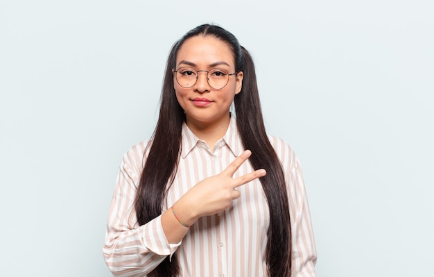 Femme latine se sentant heureuse, positive et réussie, avec la main en forme de v sur la poitrine, montrant la victoire ou la paix