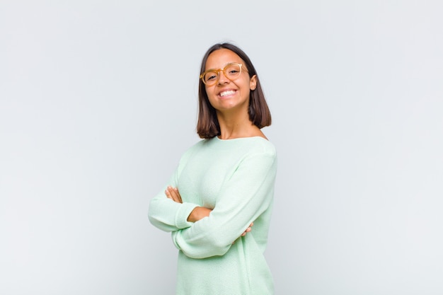 Femme latine souriant à l'avant avec les bras croisés et une expression heureuse, confiante et satisfaite, vue latérale