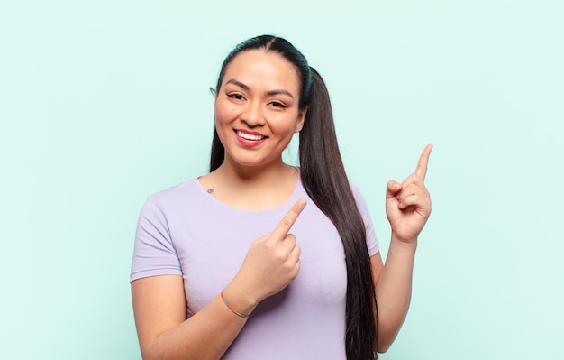 Femme latine souriant joyeusement et pointant vers le côté et vers le haut avec les deux mains montrant l'objet dans l'espace de copie