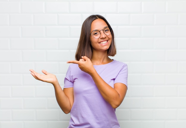 Femme latine souriant joyeusement et pointant vers l'espace de copie sur la paume sur le côté, montrant ou annonçant un objet