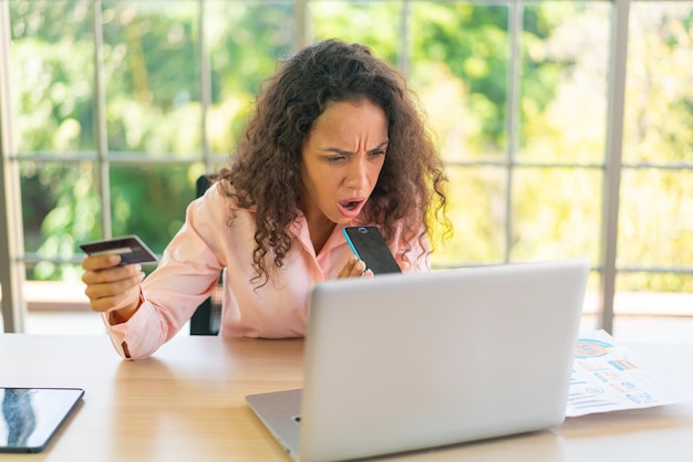 Femme latine travaillant avec la main tenant la carte sur l'espace de travail à la maison