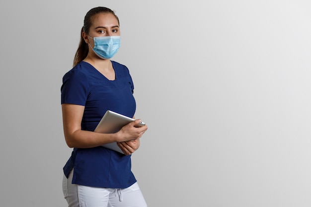 Femme latine en uniforme d'infirmière portant un masque facial et un écran facial tenant une tablette numérique