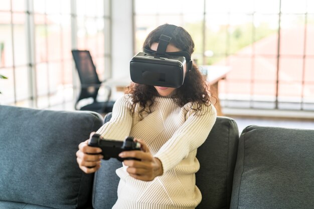 Femme latine utilisant un casque de réalité virtuelle sur un canapé à la maison