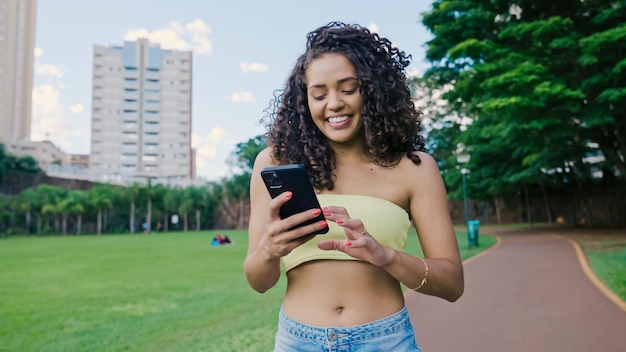 Femme latine utilisant un smartphone dans le parc. Brésilienne.