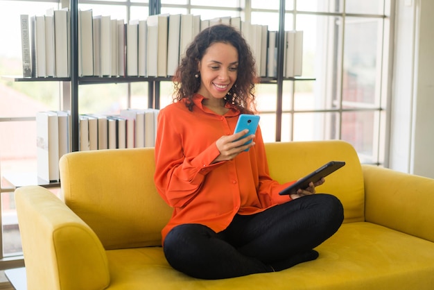 Femme latine utilisant un téléphone portable ou un smartphone et tenant une tablette d'avoine à la maison