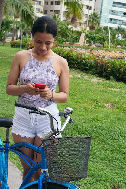 Femme latine vérifiant son téléphone portable en faisant du vélo dans la ville