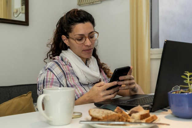 Une femme latino-américaine fait une pause et mange quelque chose en travaillant à domicile