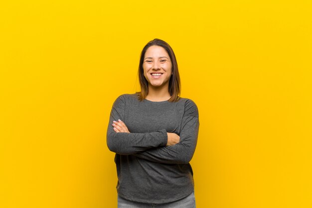 Femme latino-américaine ressemblant à un accomplisseur heureux, fier et satisfait, souriant avec les bras croisés, isolé contre le mur jaune