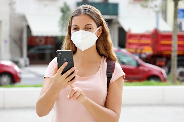 Femme latino-américaine avec un téléphone intelligent portant un masque de protection dans la rue