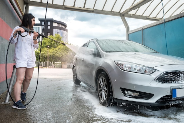 La femme lave la mousse avec de l'eau sur la voiture, nettoie et lave la voiture. un service