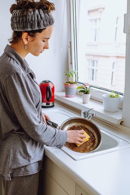 Une femme lave la vaisselle dans une cuisine avec une éponge à la main.