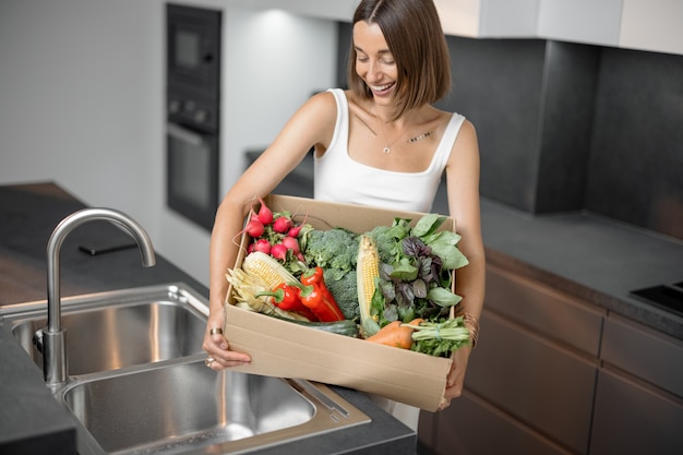 Femme avec des légumes frais emballés dans une boîte en carton à la cuisine