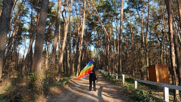 Femme lesbienne bisexuelle tenant un drapeau LGBT arc-en-ciel et marchant dans la forêt et célébrant un défilé gay Journée de la bisexualité ou Journée nationale du coming out pendant le mois de la fierté