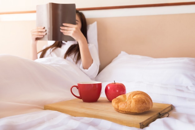 Femme à lire et à boire du café au lit pendant le matin