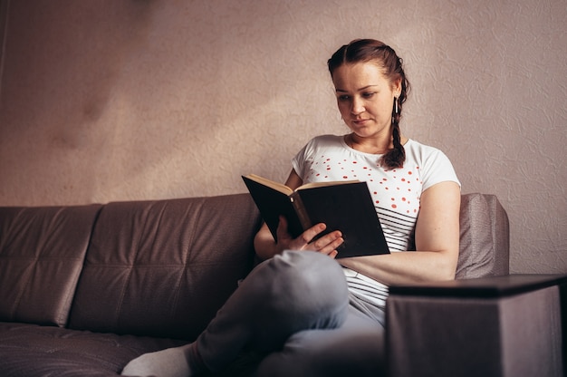 Femme lisant un livre assis sur le canapé à la maison