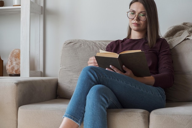 Femme lisant un livre assis dans un canapé à la maison