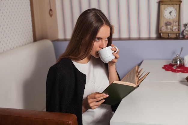 Femme lisant un livre au café et buvant du thé