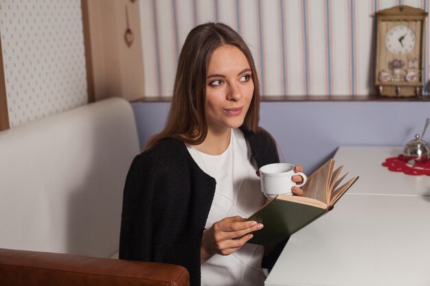 Femme lisant un livre au café et buvant du thé