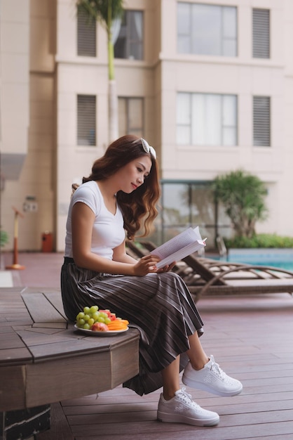 Femme lisant un livre près de la piscine d'eau.