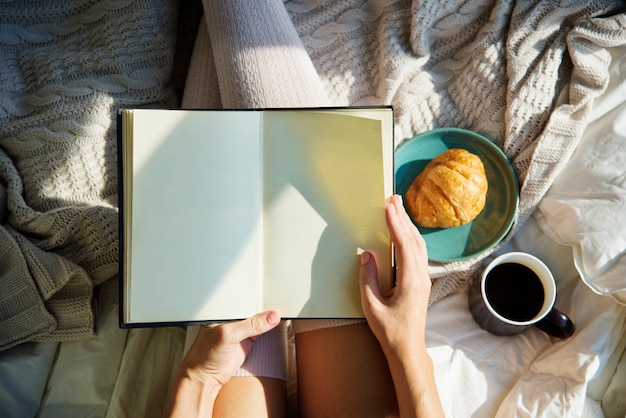 Femme lisant un livre roman sur le lit petit déjeuner