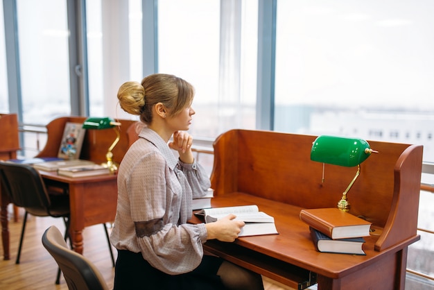 Femme lisant à la table dans la bibliothèque universitaire