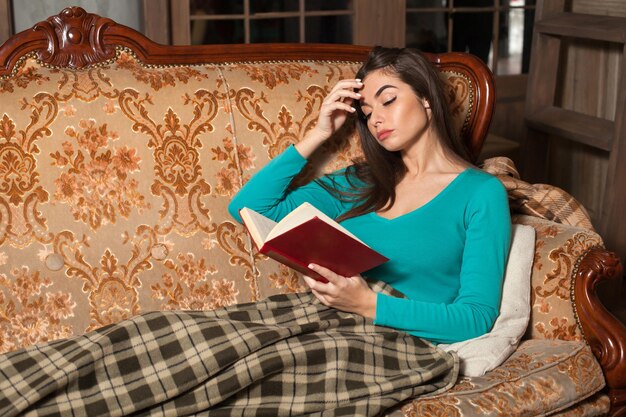 La femme lit un livre sur le beau canapé avec un plaid carré