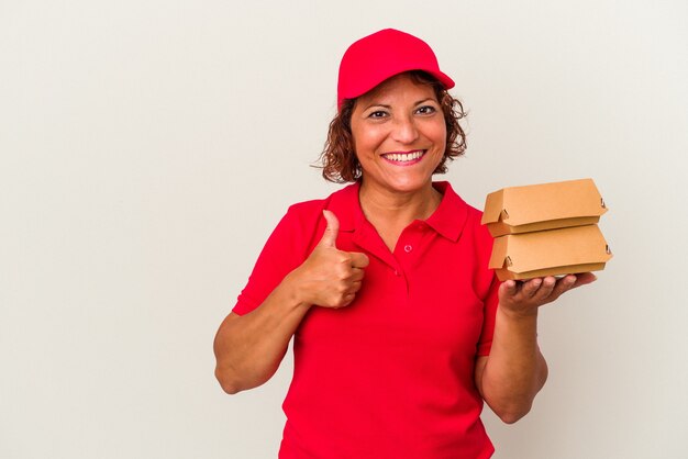 Femme de livraison d'âge moyen prenant des burguers isolés sur fond blanc souriant et levant le pouce vers le haut