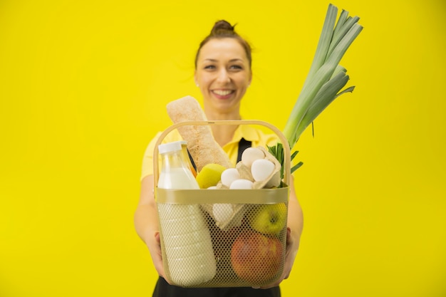 Femme de livraison détient panier avec épicerie sur mur jaune, espace copie