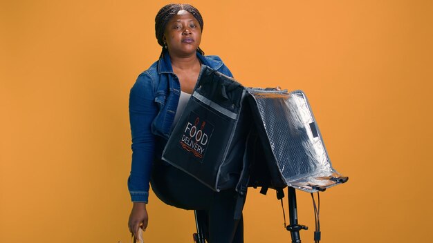 Photo une femme de livraison efficace déchargeant un fast-food après l'arrivée avec un vélo dans le quartier du client. un courrier afro-américain déballe son sac de livraison de nourriture à la destination du client.