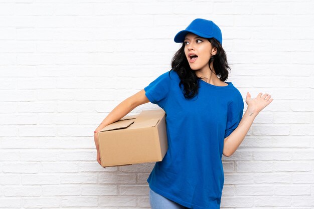 Femme de livraison jeune sur mur de briques blanches avec une expression faciale surprise