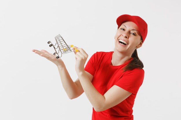 Femme de livraison en uniforme rouge isolé sur fond blanc. Coursier ou marchand féminin en casquette, t-shirt, jeans tenant un chariot d'épicerie de supermarché pour faire du shopping sur la paume. Copiez l'espace pour la publicité.