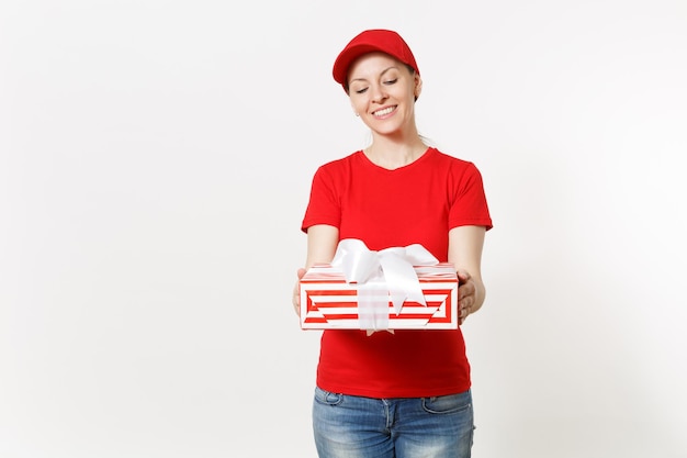 Femme de livraison en uniforme rouge isolé sur fond blanc. Femme souriante en casquette, t-shirt, jeans travaillant comme coursier ou revendeur, tenant une boîte-cadeau à rayures rouges avec cadeau. Copiez l'espace pour la publicité.