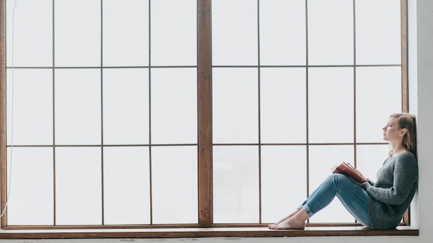 Femme avec livre au repos près de la fenêtre